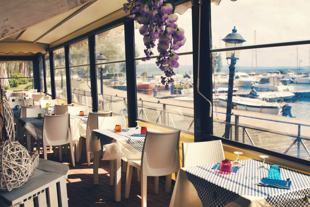 Ristorante con tavoli apparecchiati, vista sul porto.
