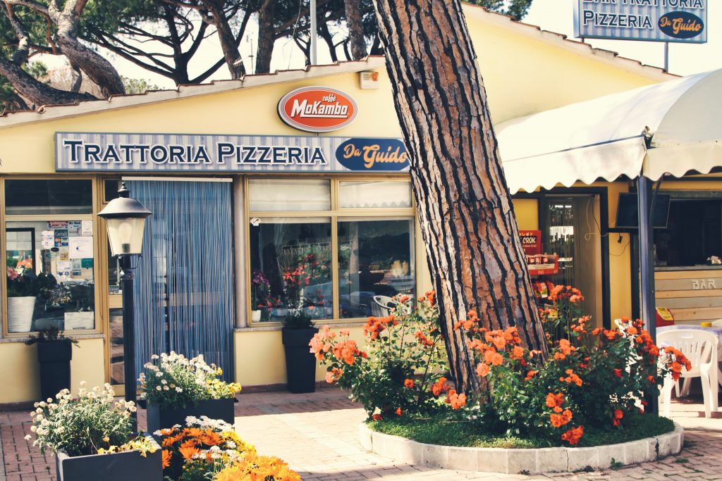 Esterno di una trattoria pizzeria con fiori colorati.