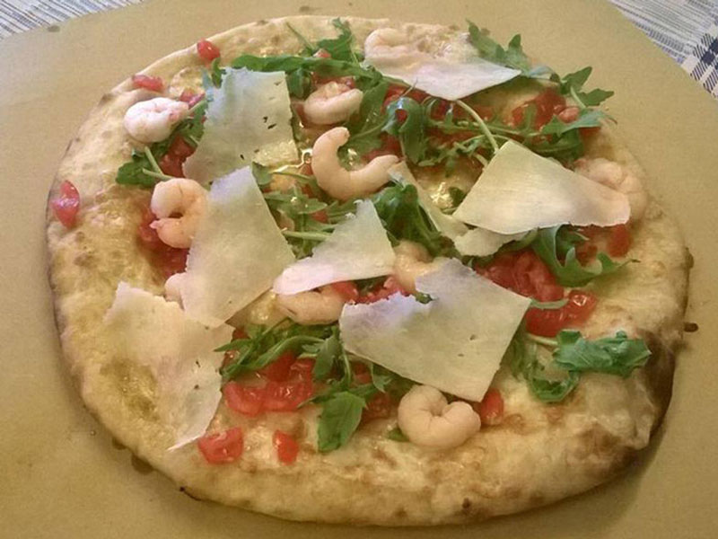 Pizza con gamberetti, rucola, pomodori e scaglie di formaggio.