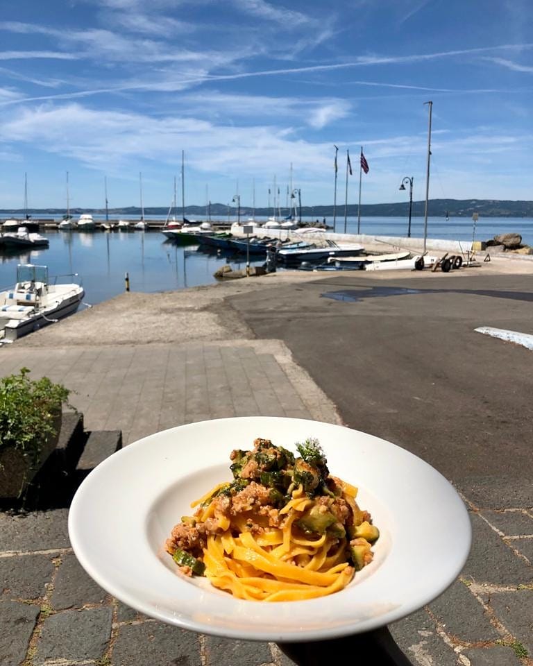 Piatto di pasta con porto e barche sullo sfondo.
