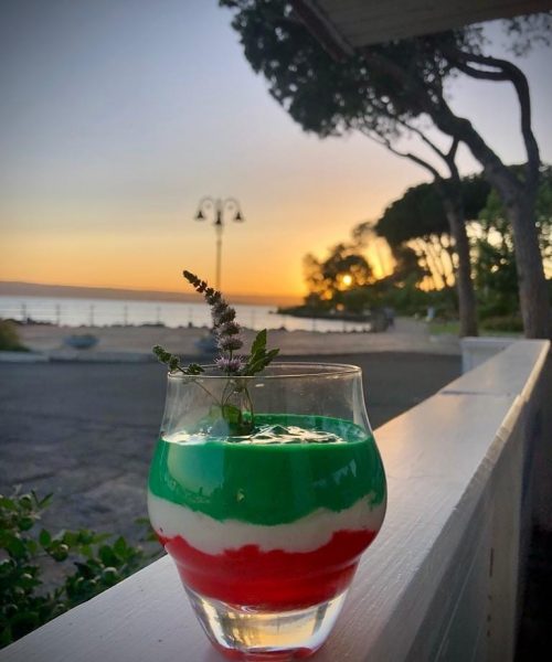 Bicchiere con dessert tricolore, sfondo tramonto sul mare.