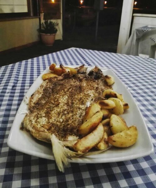 Pesce al forno con patate su tavolo a quadretti.