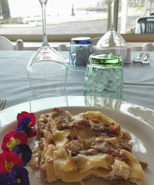 Piatto di lasagne con fiori commestibili su tavola apparecchiata.