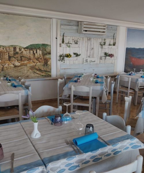 Ristorante con tavoli apparecchiati e murales alle pareti.