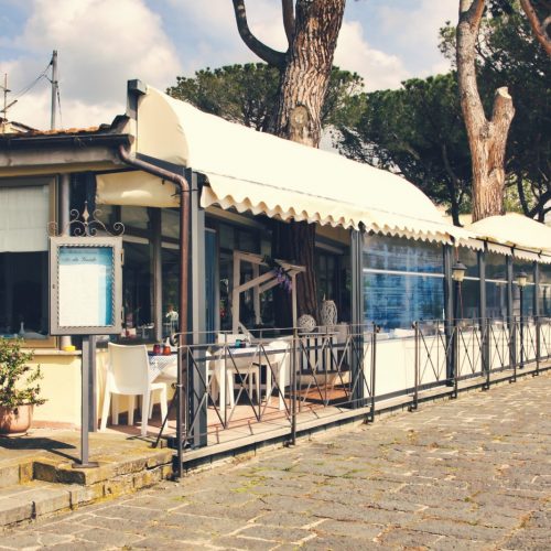 Ristorante all'aperto con veranda e tavoli apparecchiati.