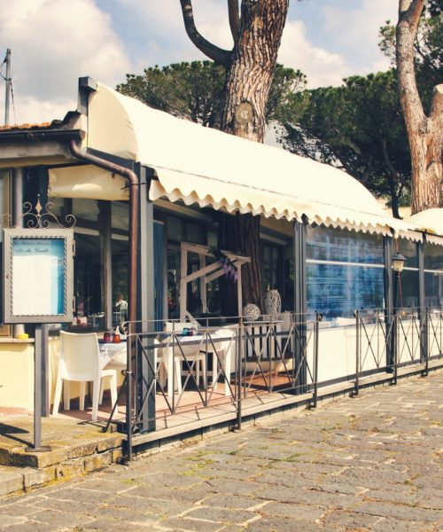 Ristorante all'aperto con veranda e tavoli apparecchiati.