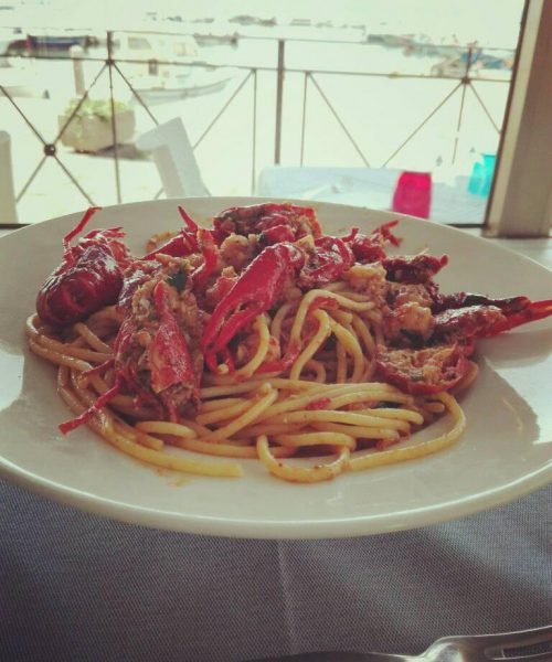 Piatto di spaghetti con astice su tavolo all'aperto.