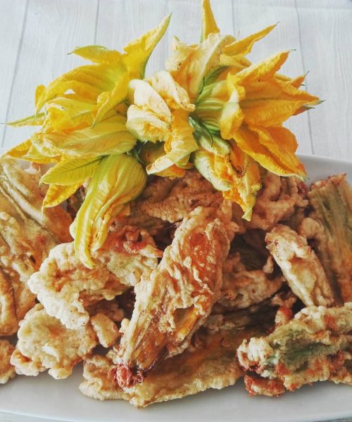 Fiori di zucca fritti su un piatto bianco.
