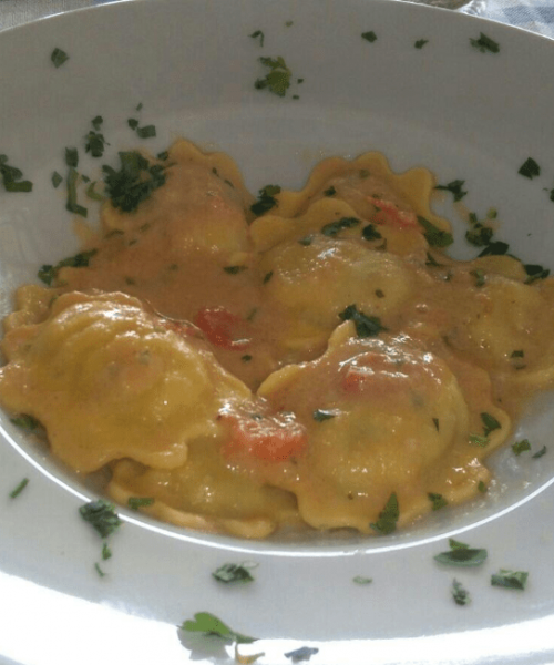 Ravioli in salsa cremosa con prezzemolo su piatto bianco.