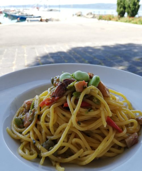 Piatto di spaghetti con verdure, vista sul mare.