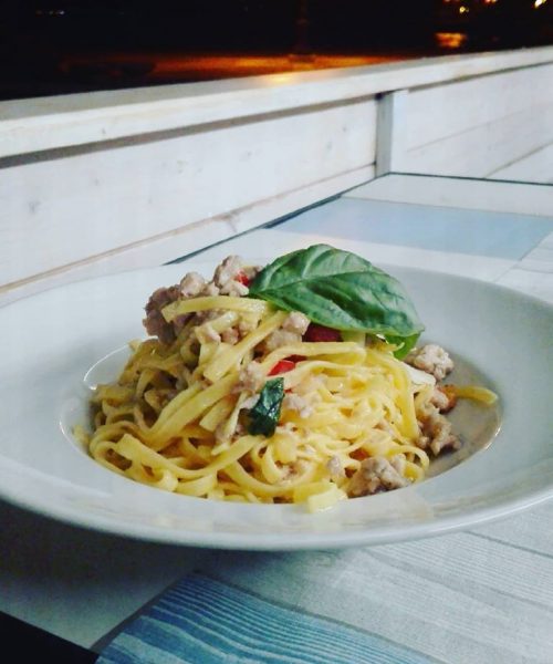 Piatto di pasta con carne e foglia di basilico.